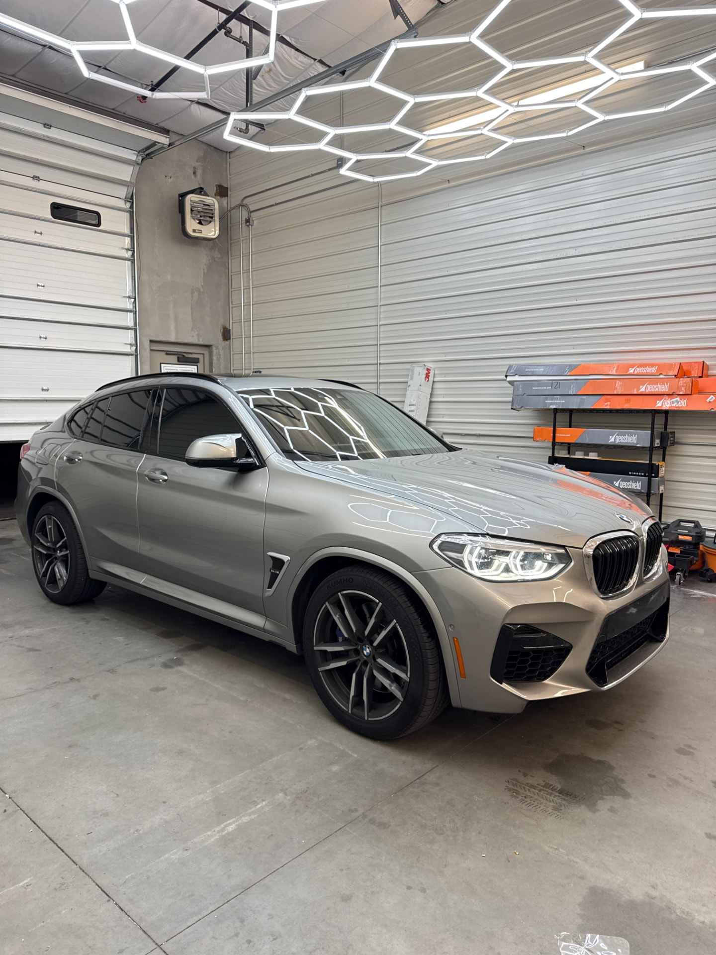 Silver BMW X4 M with ceramic window tint under the shop's hex lighting