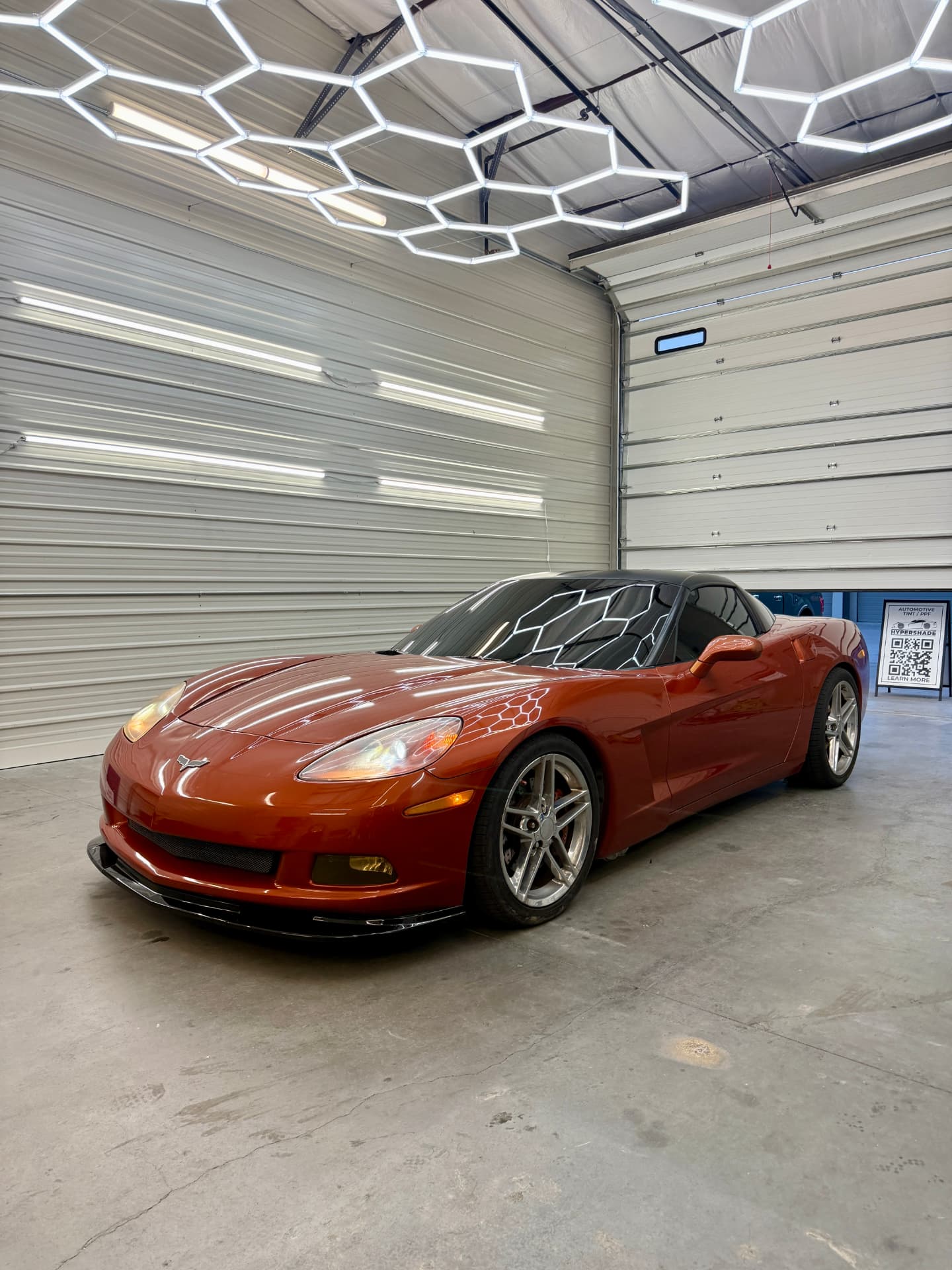 Orange Chevrolet Corvette with tinted glass under the shop's hex lighting